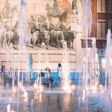 A man proposes to a woman in the background with fountains in the foreground; Five art gallery marriage proposal ideas.