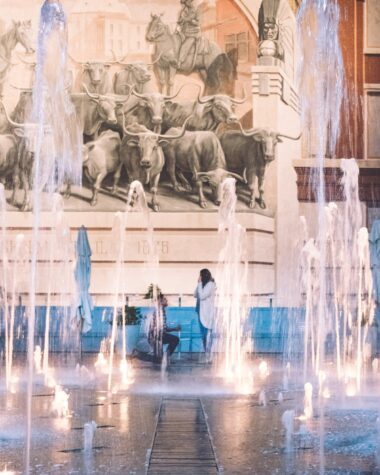 A man proposes to a woman in the background with fountains in the foreground; Five art gallery marriage proposal ideas.